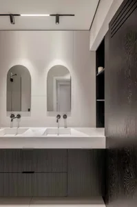 A modern minimalist bathroom featuring concrete walls, black wood paneling, and a double sink with arched mirrors.