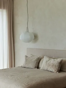 Minimalist bedroom interior with textured fabric blanket, geometric pendant light, and beige-colored bedding.