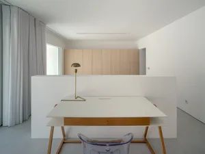 A minimalist office desk space with a white laminate top and a wooden legged chair in front of it.