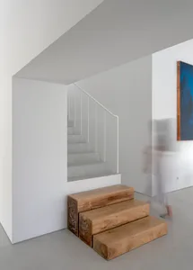 A minimalist staircase with wooden steps and a white concrete wall in a white, empty space.