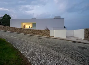 Modern residential exterior with a white stone wall and large glass windows.