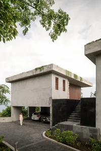 一座極簡住宅，混凝土外觀，設有遮蓋式停車位與階梯。
