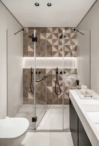 Modern bathroom with geometric patterned ceramic tiles on the wall, glass shower enclosure, and minimalist design elements.