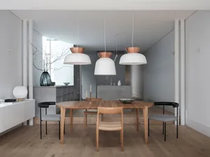 Modern dining room with wooden table, concrete wall, and copper pendant lights.