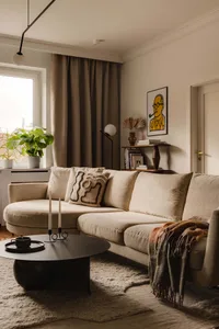A modern living room featuring a fabric couch in a neutral color, with a round coffee table, potted plants, and a painting on