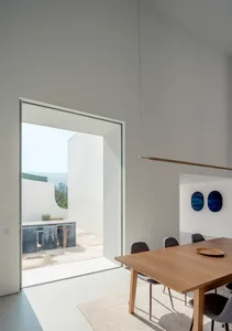 A modern minimalist dining room featuring a wooden table, chairs, and a large window.