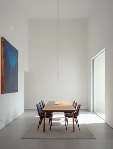 Modern minimalist dining room with a wooden table and chairs, featuring a large abstract painting and natural light streaming