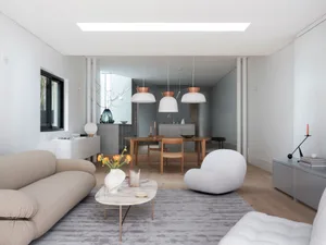 A minimalist living room with a modern design featuring a beige sofa, a round marble coffee table, and a white armchair.