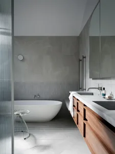 Modern minimalist bathroom featuring a grey concrete floor, grey tile walls, and a white bathtub.