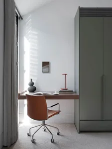 A minimalist home office setup with a wooden desk, brown leather chair, and white walls.