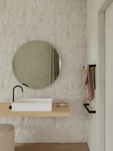 Modern minimalist bathroom with stone walls, a round mirror, a rectangular sink, and a towel bar.