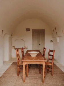 A minimalist dining room featuring a wooden table with a large bowl on it, surrounded by wooden chairs.