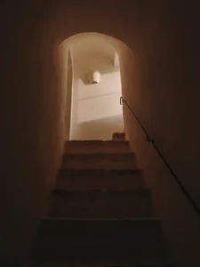 A narrow stone staircase with a metal railing in an indoor building.