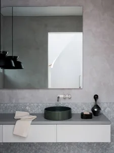 A minimalist modern bathroom featuring a sleek black sink, white cabinets, and a large rectangular mirror with concrete textu