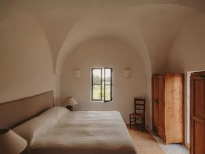 A minimalist bedroom with concrete flooring, a bed, and simple furniture.