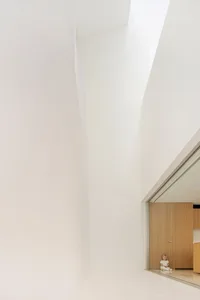 A minimalist living room with white concrete walls and a high ceiling.