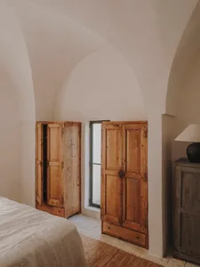 A minimalist bedroom with wooden furniture, white bedding, and a window with a view of the outdoors.