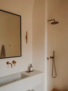 Modern minimalist bathroom featuring a concrete countertop sink, brass fixtures, and a mounted shower head.