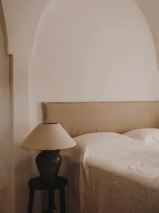 A minimalist bedroom featuring a bed with beige linen bedding and a ceramic lamp on a small side table.