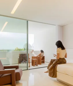 A minimalist bedroom with white walls and floor, featuring a wooden bed frame and large glass window.