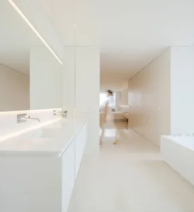 Modern minimalist bathroom with white marble flooring, fixtures, and a large mirror with lighting along the back edge.