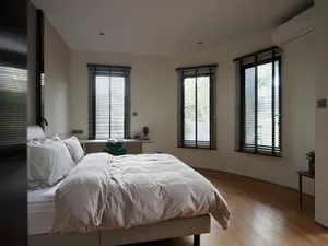 Minimalist bedroom featuring a bed with neutral-toned bedding, wooden flooring, and metal headboard.