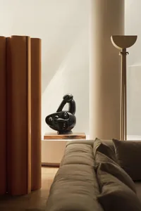 A modern living room with a wooden sofa and a black bird sculpture on a shelf.