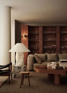 Modern living room with a marble coffee table, wooden sofa, and shelves filled with glasses.