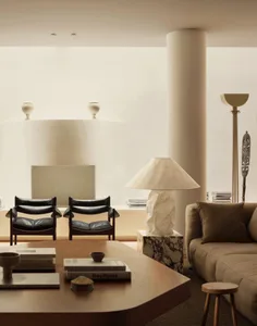 A modern living room featuring neutral-toned leather furniture, marble accents, and a concrete column.