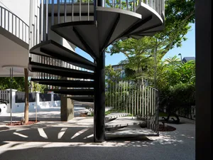 Outdoor spiral staircase with black metal railings and steps, framed by greenery and trees.