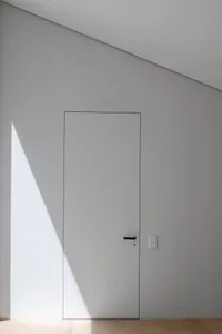 A minimalist white door with a light shadow cast on it, set against a white wall with vertical paneling.