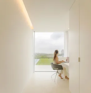 A modern home office with light wood elements and floor-to-ceiling windows overlooking a landscape.