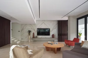 A modern living room with a marble accent wall, a wooden coffee table, and a television on a white cabinet.