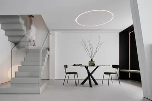 A minimalist dining area featuring a metallic table and chairs, with a circular light fixture and a person descending a stair