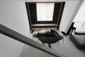 A modern minimalist living space featuring a sleek, round table with a vase and books, a comfortable seat by a window, and co