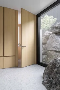 Modern entrance with wooden door, concrete floor, and rock wall