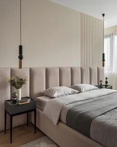 A minimalist bedroom with a beige fabric headboard and a grey bedspread, featuring modern pendant lights and nightstands with