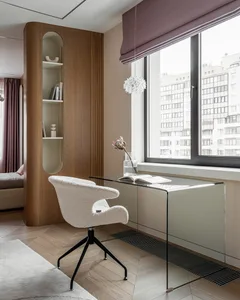 A modern interior design featuring a glass desk and a cozy white chair.