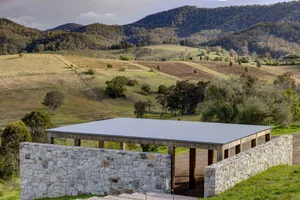 A modern industrial-style building exterior with a metal roof and stone walls in a rural setting.
