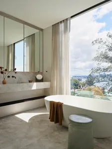 Modern minimalist bathroom featuring a marble bathtub and sink, with a large window showcasing an ocean view.