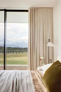 Modern minimalist bedroom featuring linen blinds and a serene view of a vineyard.