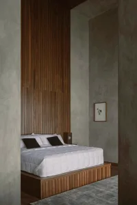 A minimalist bedroom with a wooden platform bed and a tall wooden panel wall.