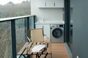 Balcony laundry room with modern wood and metal furniture, glass railing, and white appliances.