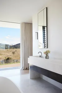 A modern bathroom featuring marble countertops and a serene view of nature through large windows.