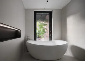 A modern minimalist bathroom with a white porcelain bathtub, grey porcelain tiles, and a large window with a view of greenery
