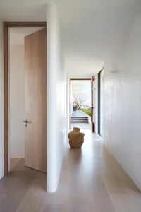A modern interior hallway with wooden flooring and walls, featuring an open door and a vase on the floor.
