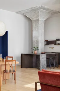 A modern kitchen with exposed concrete columns and a marble counter, featuring an open-plan living area.