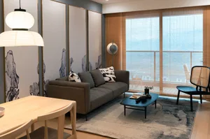 A modern living room with a gray sofa, black and white patterned pillows, and a wooden dining table with white chairs.