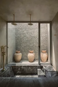 A modern marble bathroom with three large vases and two shower heads.