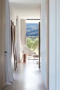 Minimalist modern living room with white furniture and wooden elements, featuring a view of greenery outside through the larg